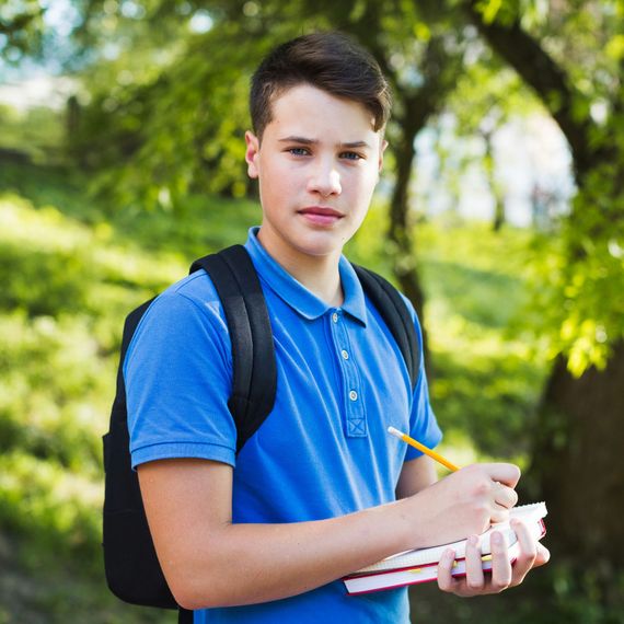 Étudiant en chemise bleue et sac à dos, tenant un cahier et un crayon à l'extérieur