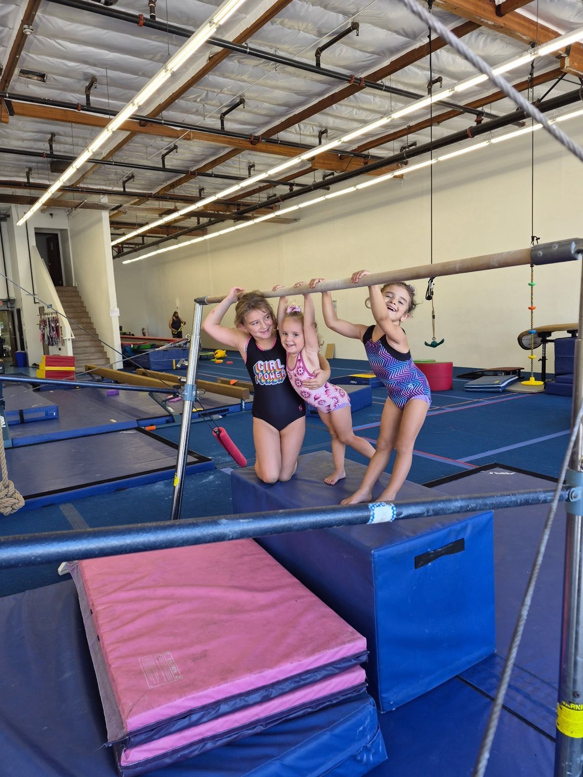 Three children smiling together at a gymnastics bar at GRIT Gymnastics.