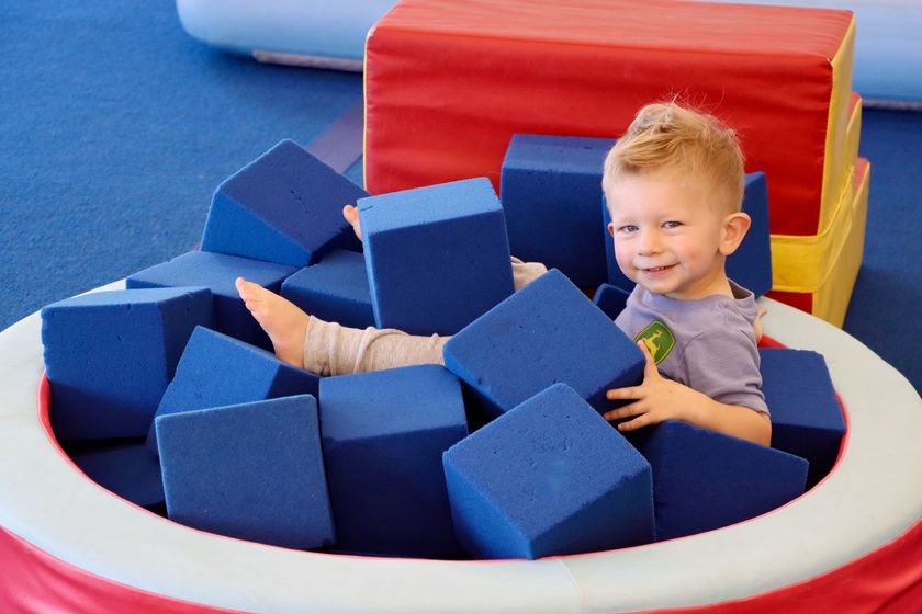 Child playing in a foam pit with blue blocks and red-and-yellow padded walls