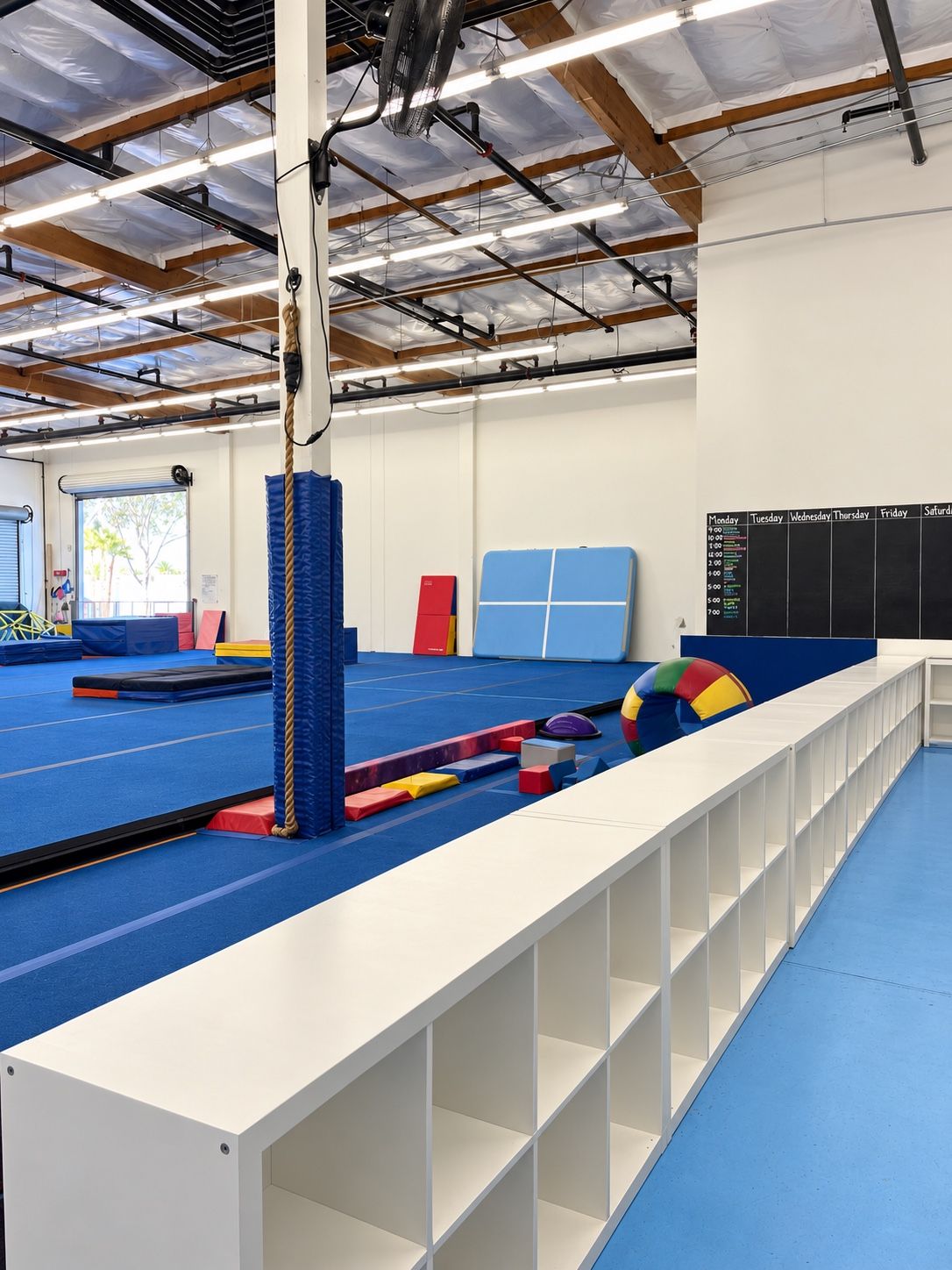Long white cubbies beside the blue gymnastics floor.
