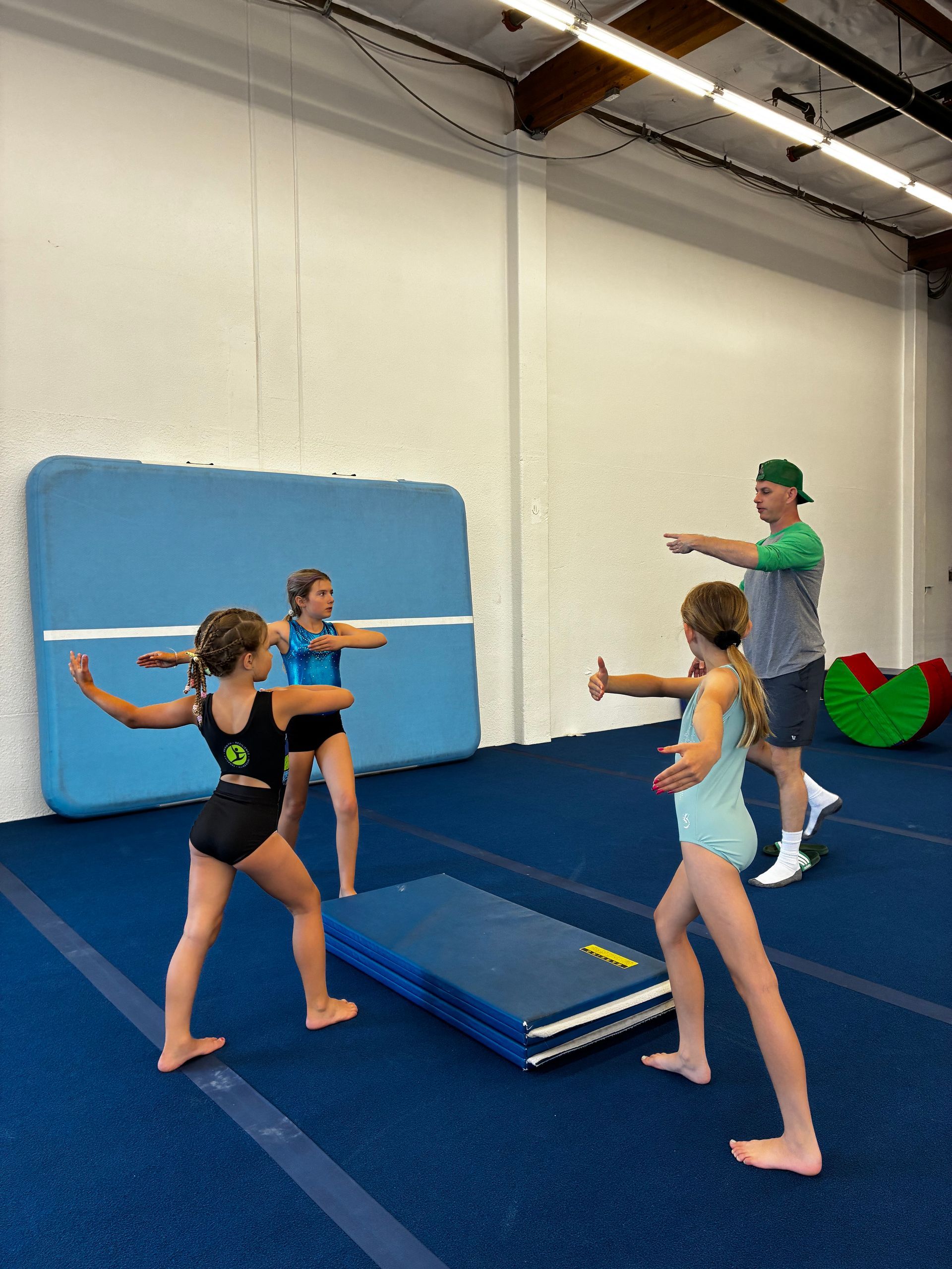 Baby learning to walk with a woman in a gymnastics studio, blue floor.