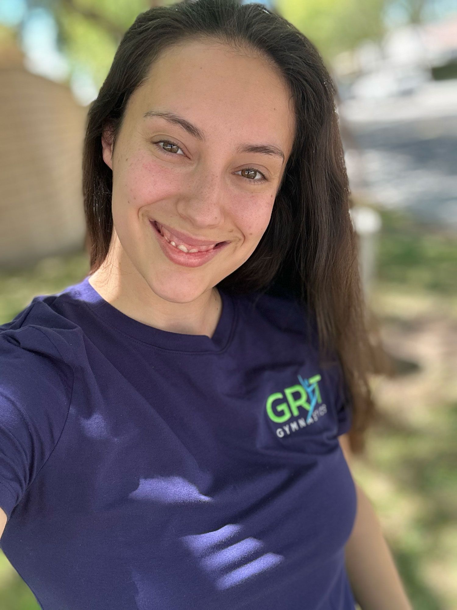 Woman in blue shirt smiles outdoors. Shirt has 