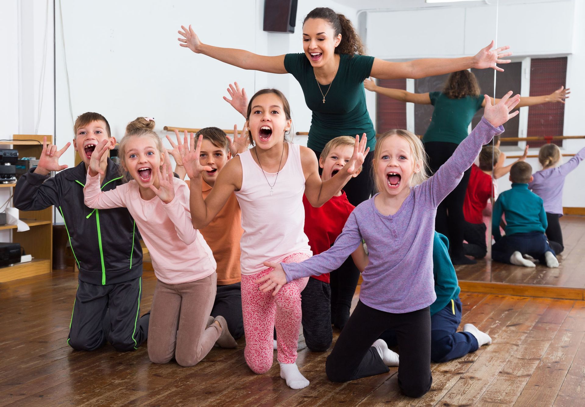 Children and instructor in a dance studio, arms raised in excitement.