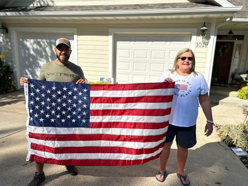 Two people holding a large American flag in a driveway in front of a house