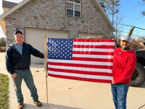 Two people holding an American flag in a driveway in front of a house