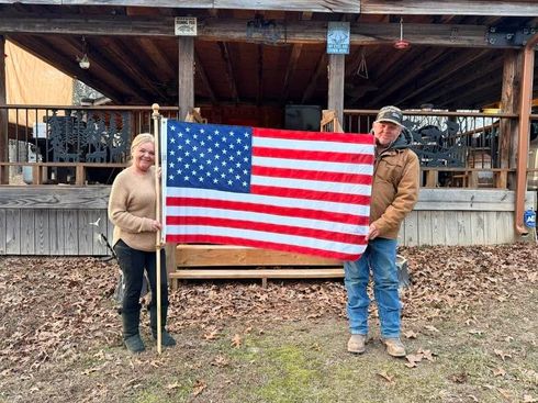 Two people holding a U.S. flag in front of a wooden pavilion outdoors