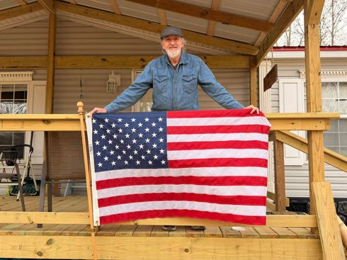 Man holding a large American flag on a wooden porch