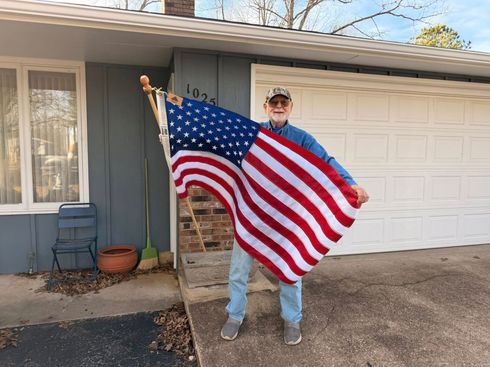 Person standing outside a garage holding a large American flag