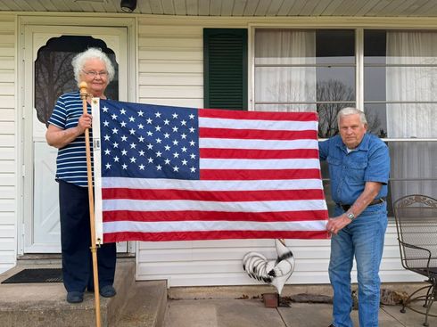Two people holding a large American flag in front of a house
