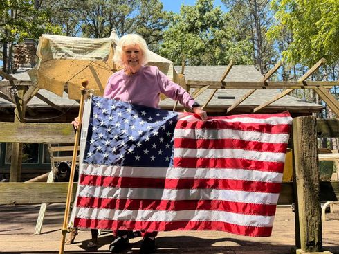 Person holding a large American flag in front of a wooden structure outdoors