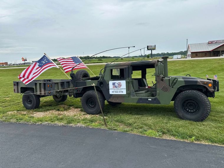 Military Humvee with American flags parked on grass beside a road