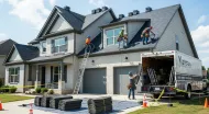 Roofers working on a gray two-story house with a ladder and truck in the driveway.