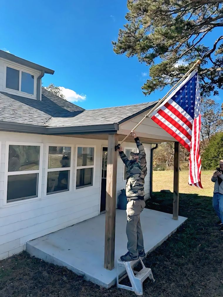 Person on a step stool hanging an American flag outside a white house.