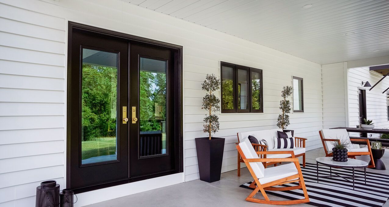 Covered porch with black double doors, white siding, and outdoor seating with striped rug