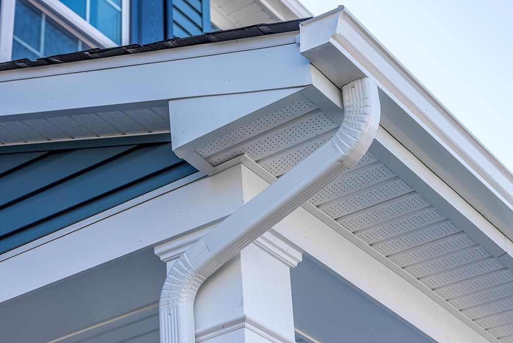 Close-up of white gutters and downspouts on a house roof edge with blue siding