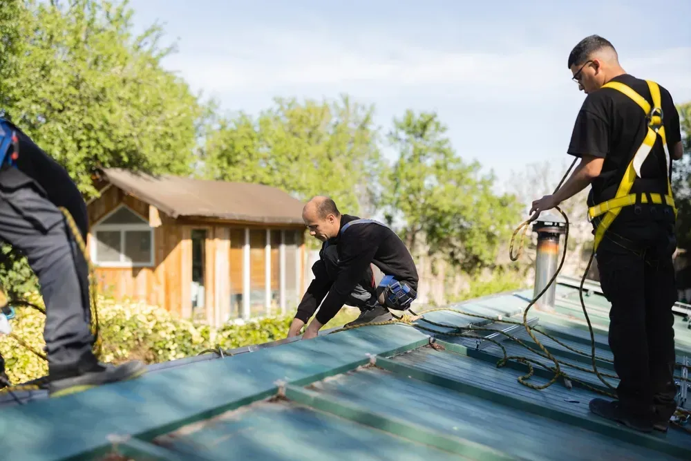 Workers installing roofing material on a house roof in a sunny backyard