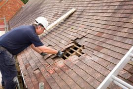Worker cutting a damaged roof shingle on a steep tiled roof with power tools