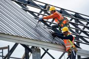 Two roofers in orange safety vests and helmets installing metal roofing on a building frame