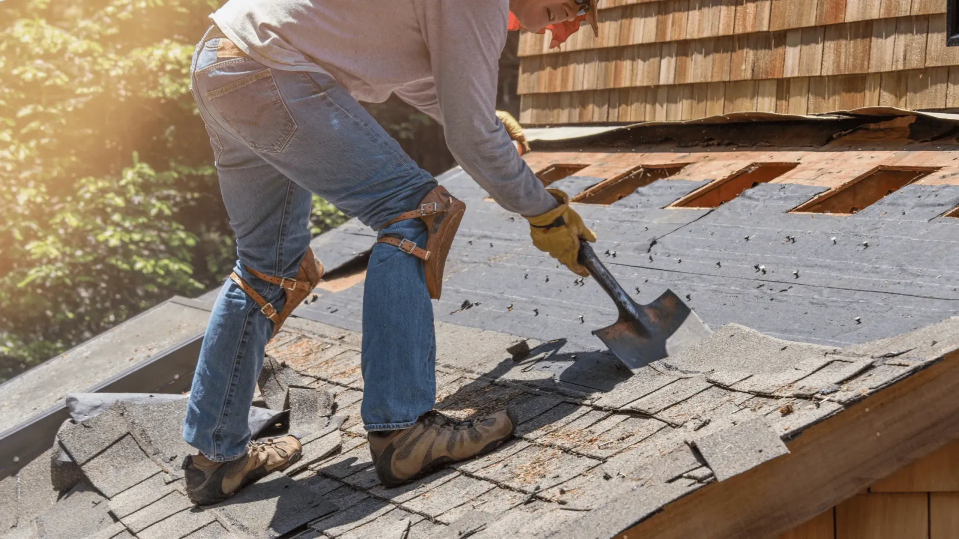 Worker removing old shingles from a roof with a shovel, sunlight on the rooftop