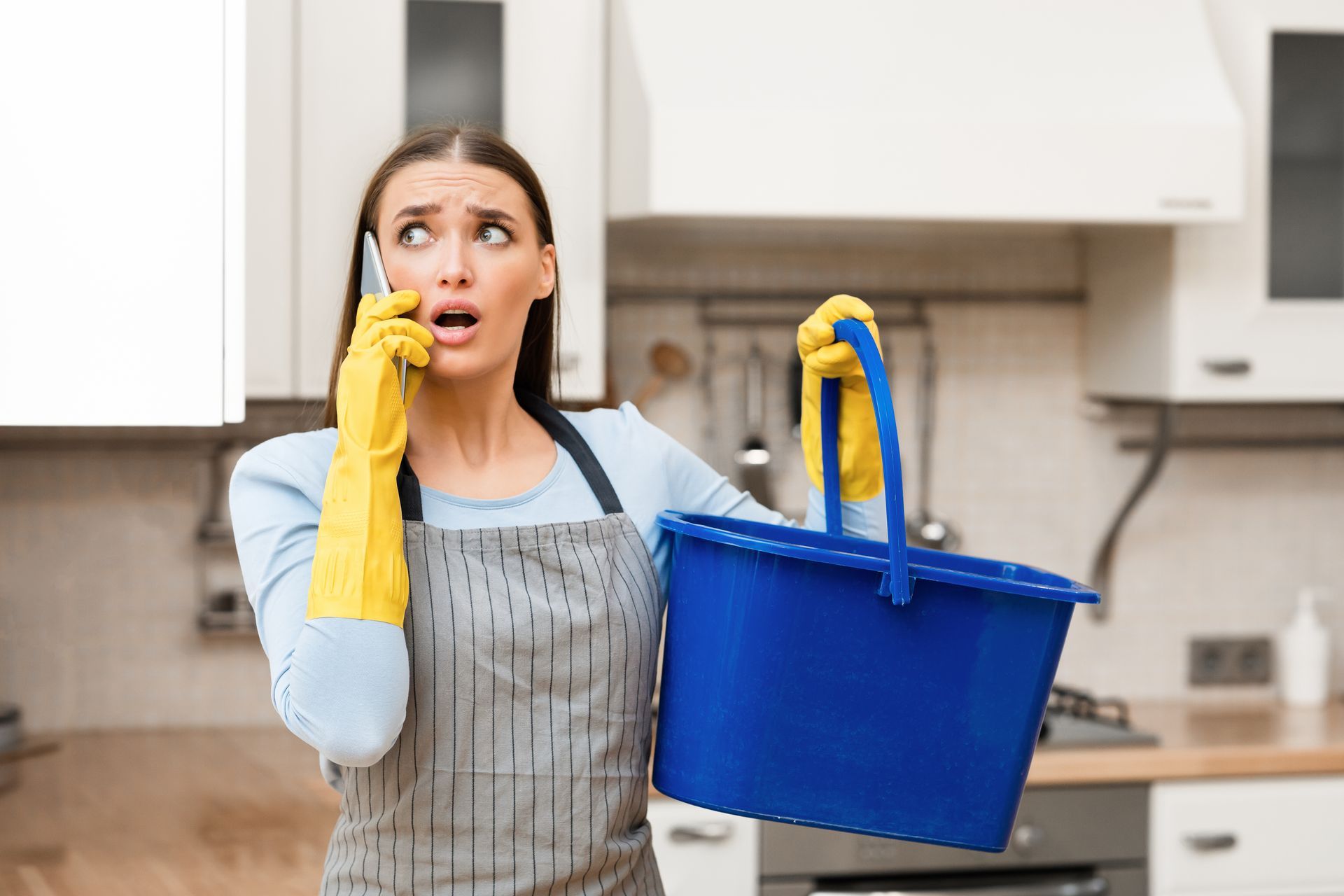 Scared young woman calling plumber holding bucket.