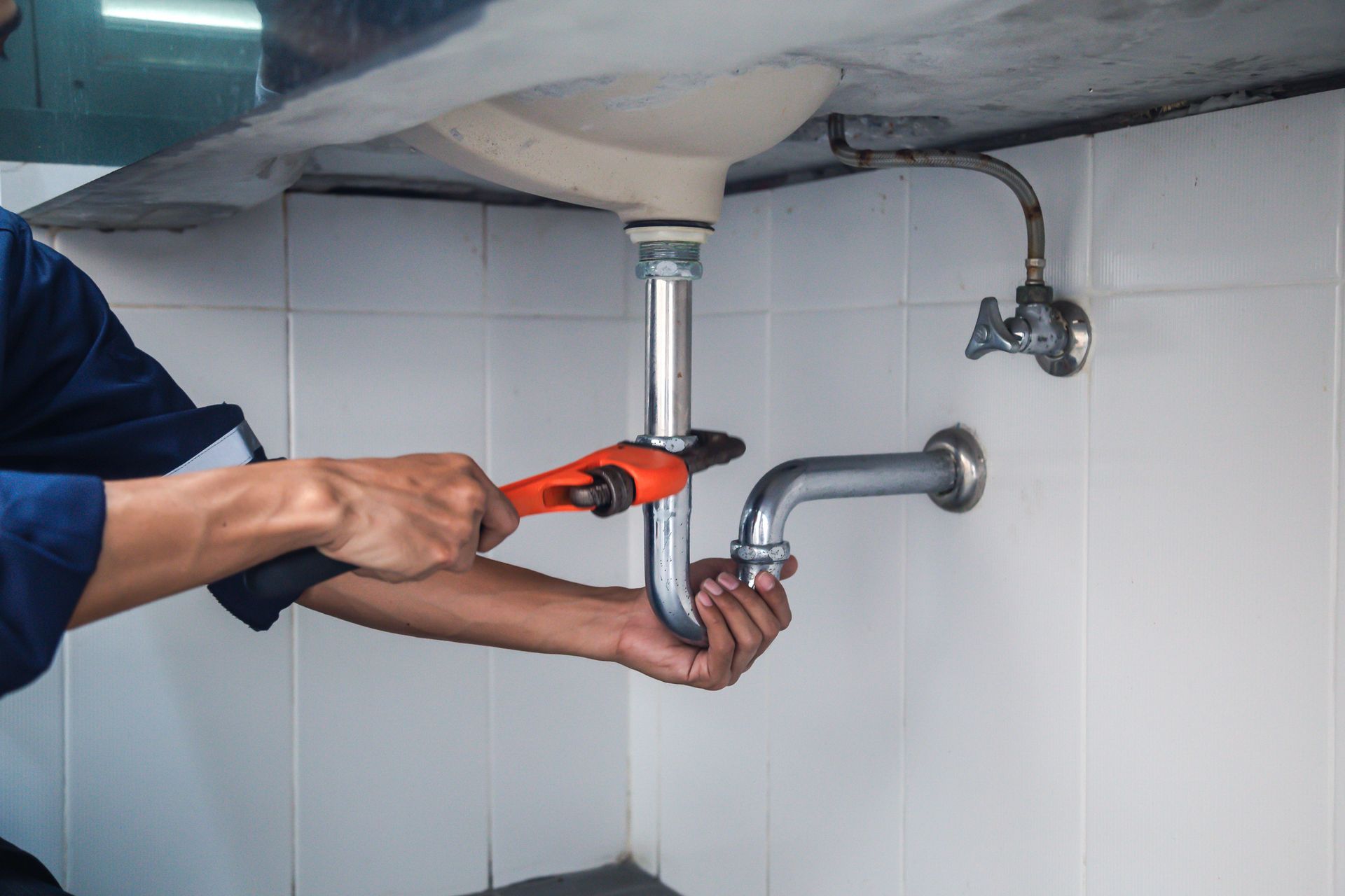 Plumber using a wrench to work on a sink drainpipe in a bathroom.