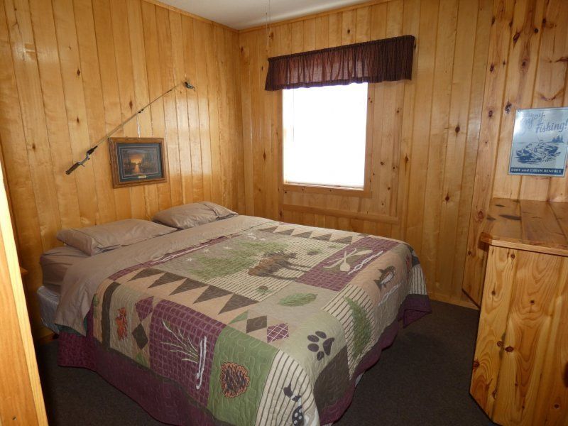Cozy wood-paneled bedroom with a bed, quilted coverlet, and a small window with a valance.