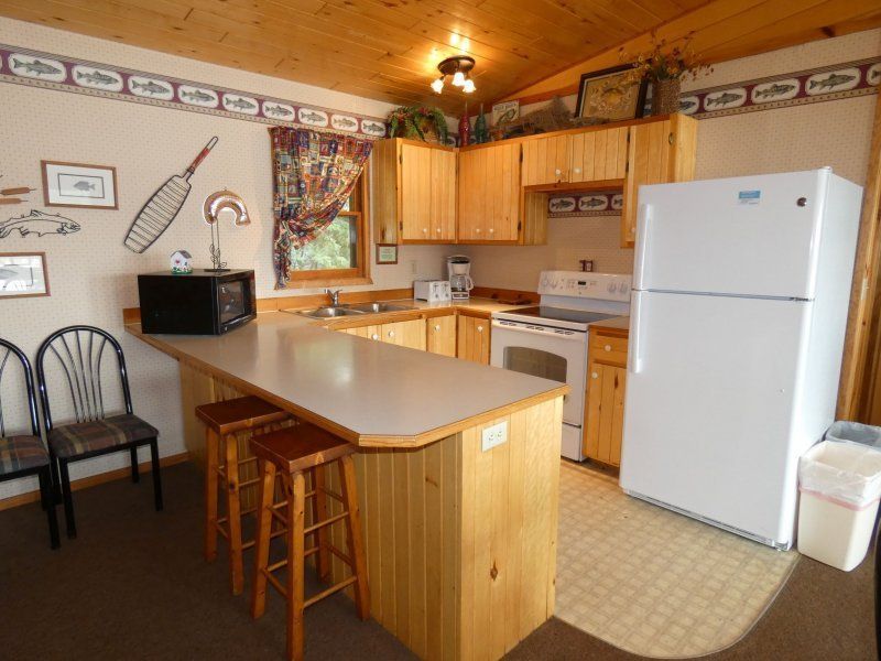 Cozy wood-paneled kitchen with island, stools, white fridge, stove, and dining chairs