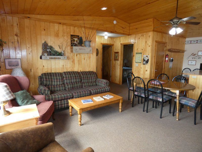 Cozy wood-paneled living room with sofas, coffee table, dining set, and ceiling fan
