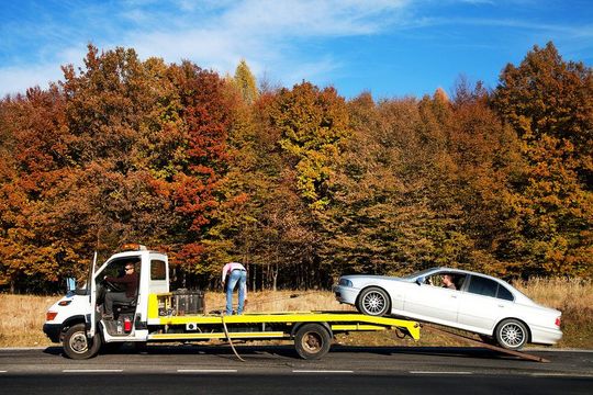 A tow truck is towing a white car on the side of the road.