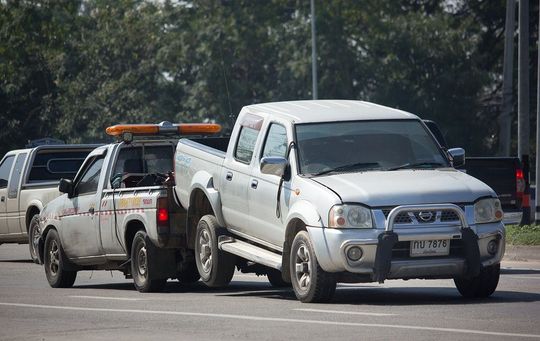 A tow truck is towing a white truck down the road.