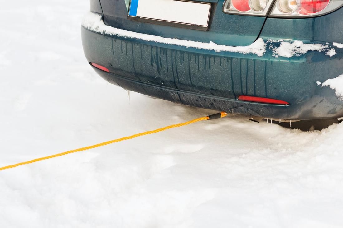 A car is stuck in the snow with a yellow rope attached to it.