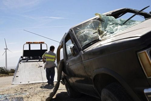 A man is standing next to a broken down car on a tow truck.