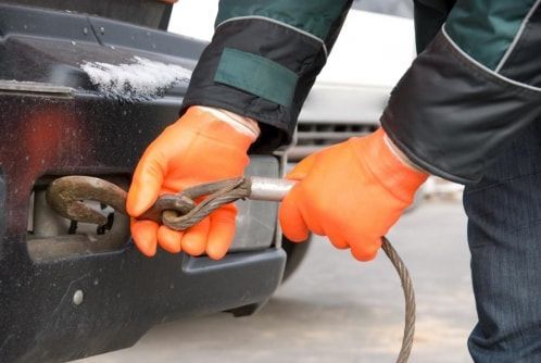 A person wearing orange gloves is towing a car