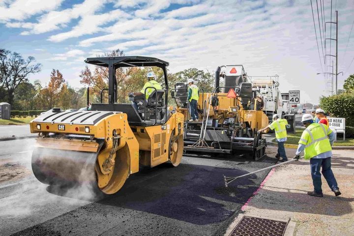 Road paving crew using yellow rollers and asphalt machine on a street under a cloudy sky
