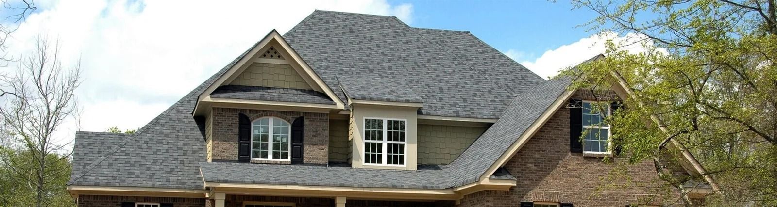 Brick house with gray shingled roof and dormer windows under a clear blue sky
