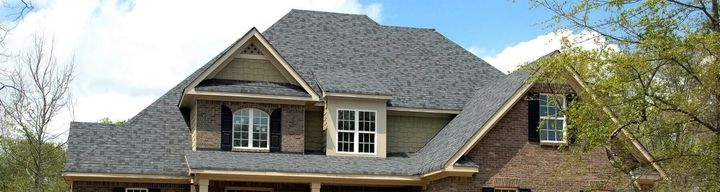 Brick house with gray shingle roof and dormer windows under a clear sky