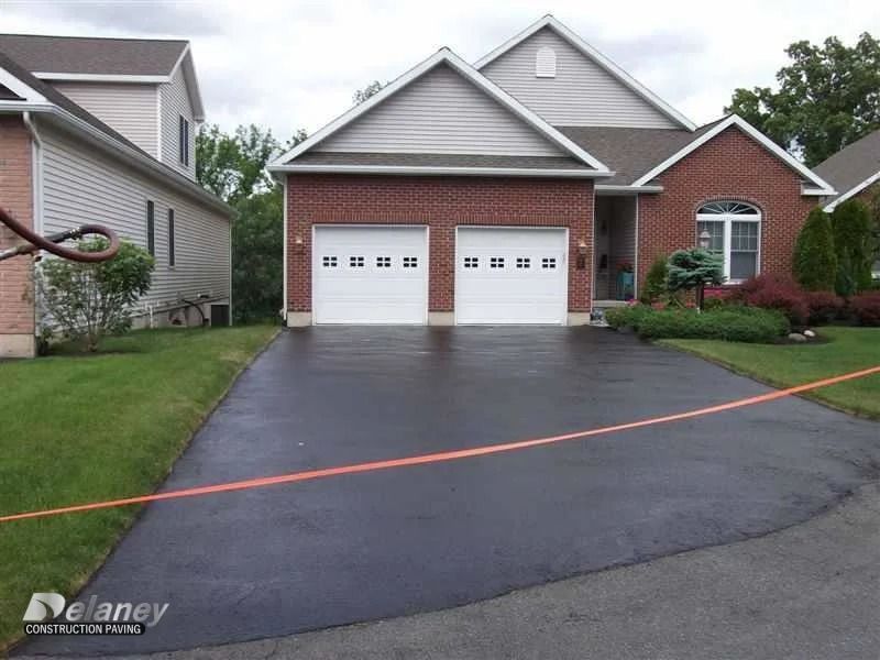Suburban brick house with two white garage doors and a freshly paved driveway, marked with orange tape.