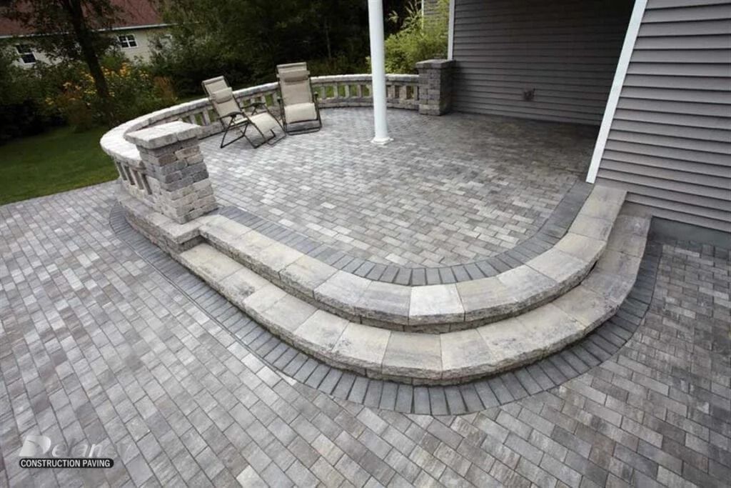 Curved stone patio with steps, gray pavers, and outdoor chairs beside a house