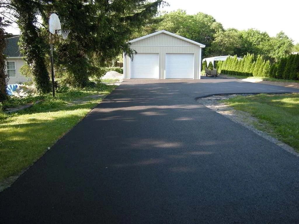 Paved driveway leading to a white two-car garage beside a green lawn and trees
