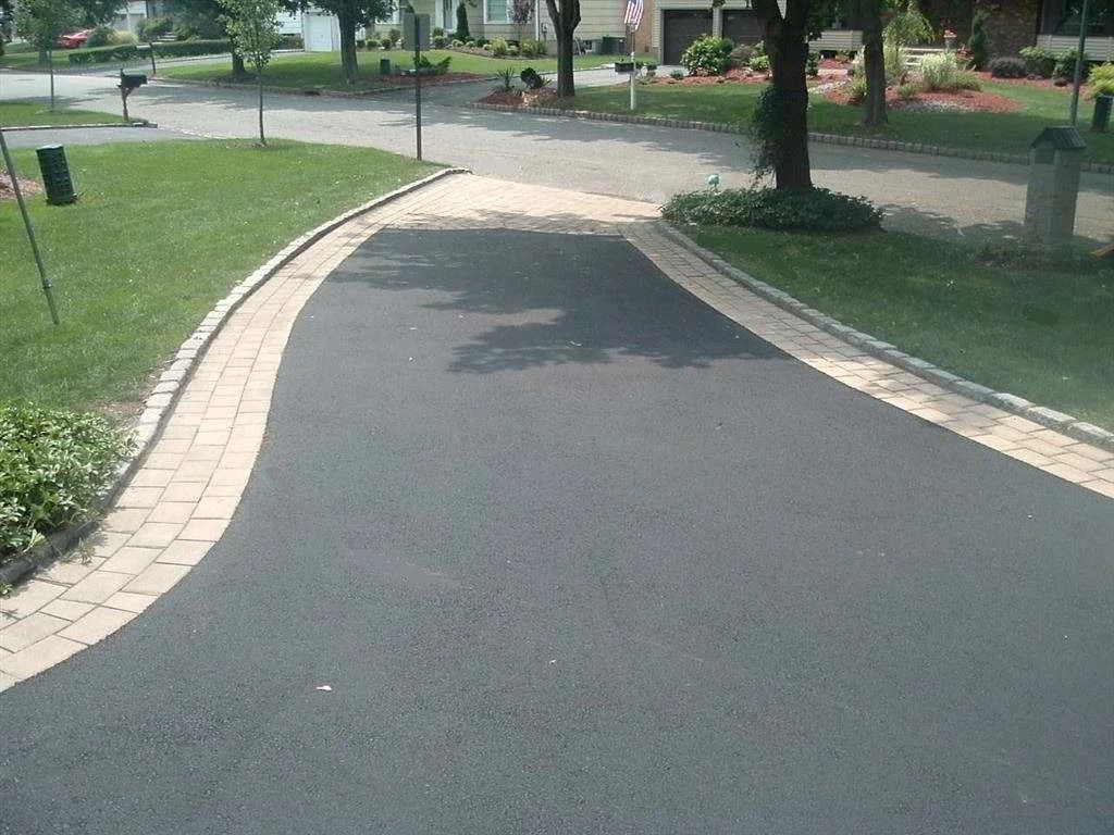 Curved asphalt path in a park with brick edging, grass, and trees on both sides