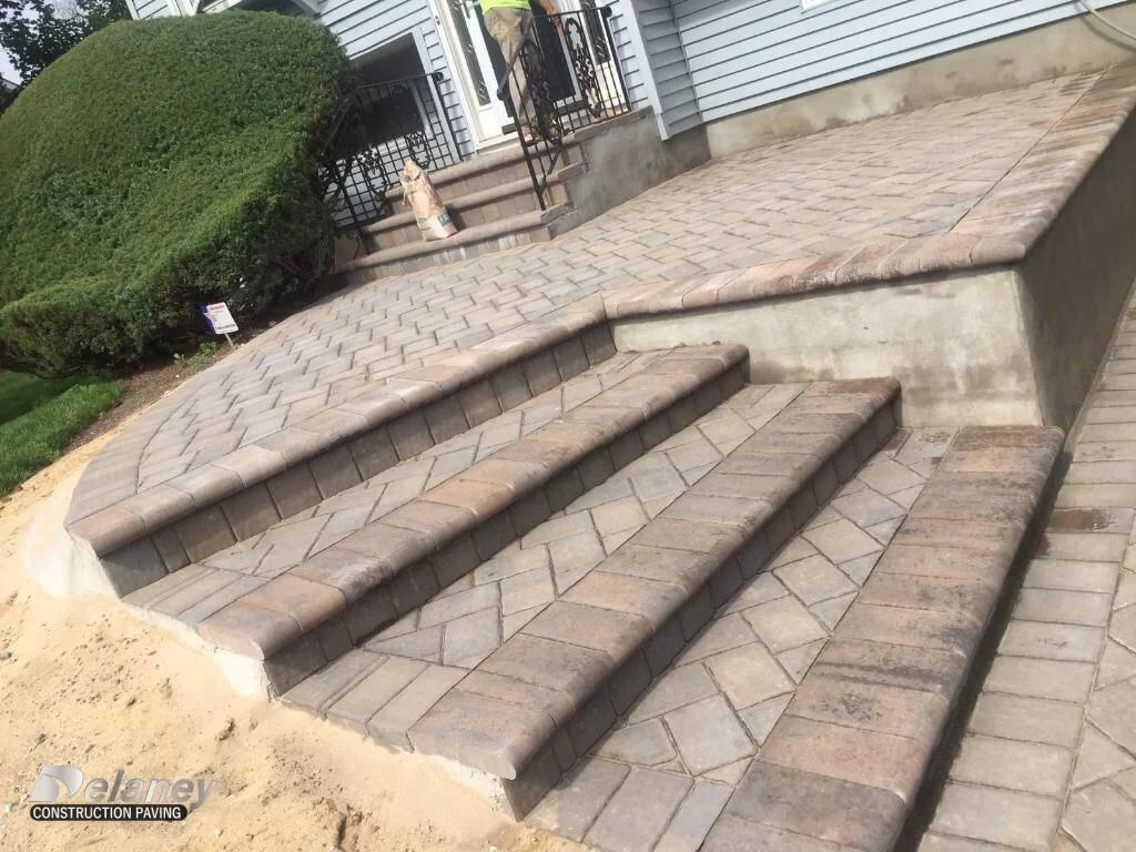Outdoor concrete steps and sloped ramp leading to a tiled platform beside a building
