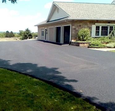 Freshly paved driveway beside a brick house with a garage and small front garden