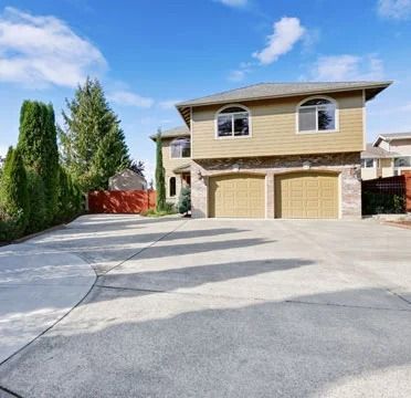 Two-story beige house with a wide concrete driveway and double garage under a blue sky