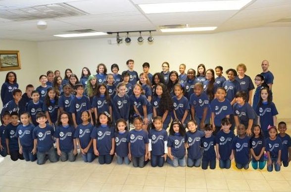 A large group of children are posing for a picture wearing blue shirts