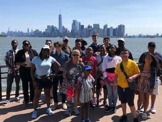 A group of people are standing in front of a body of water with a city skyline in the background.