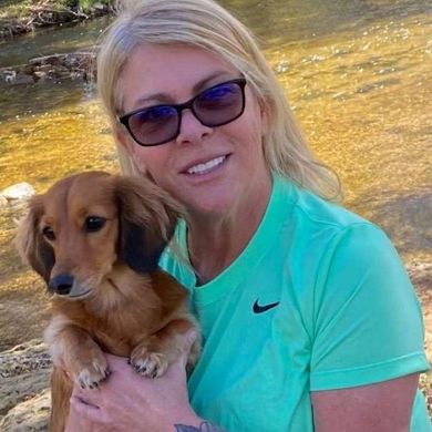 A woman in a green nike shirt is holding a small brown dog.