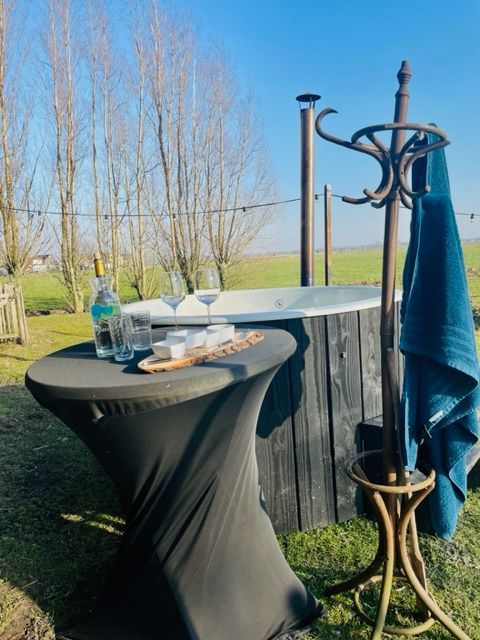Een jacuzzi in de buitenlucht met drankjes op een tafeltje, een handdoek aan de kapstok en een zonnige hemel.