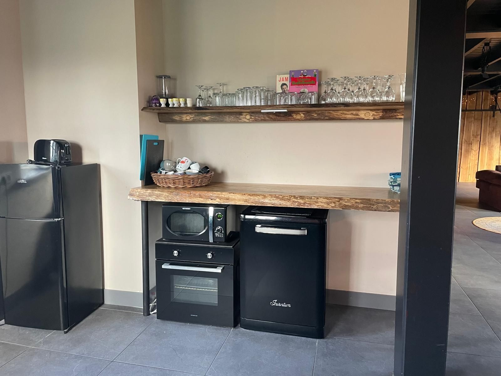 Kitchenette met zwarte apparaten, een aanrechtblad met natuurlijke randen en een houten plank voor glazen.
