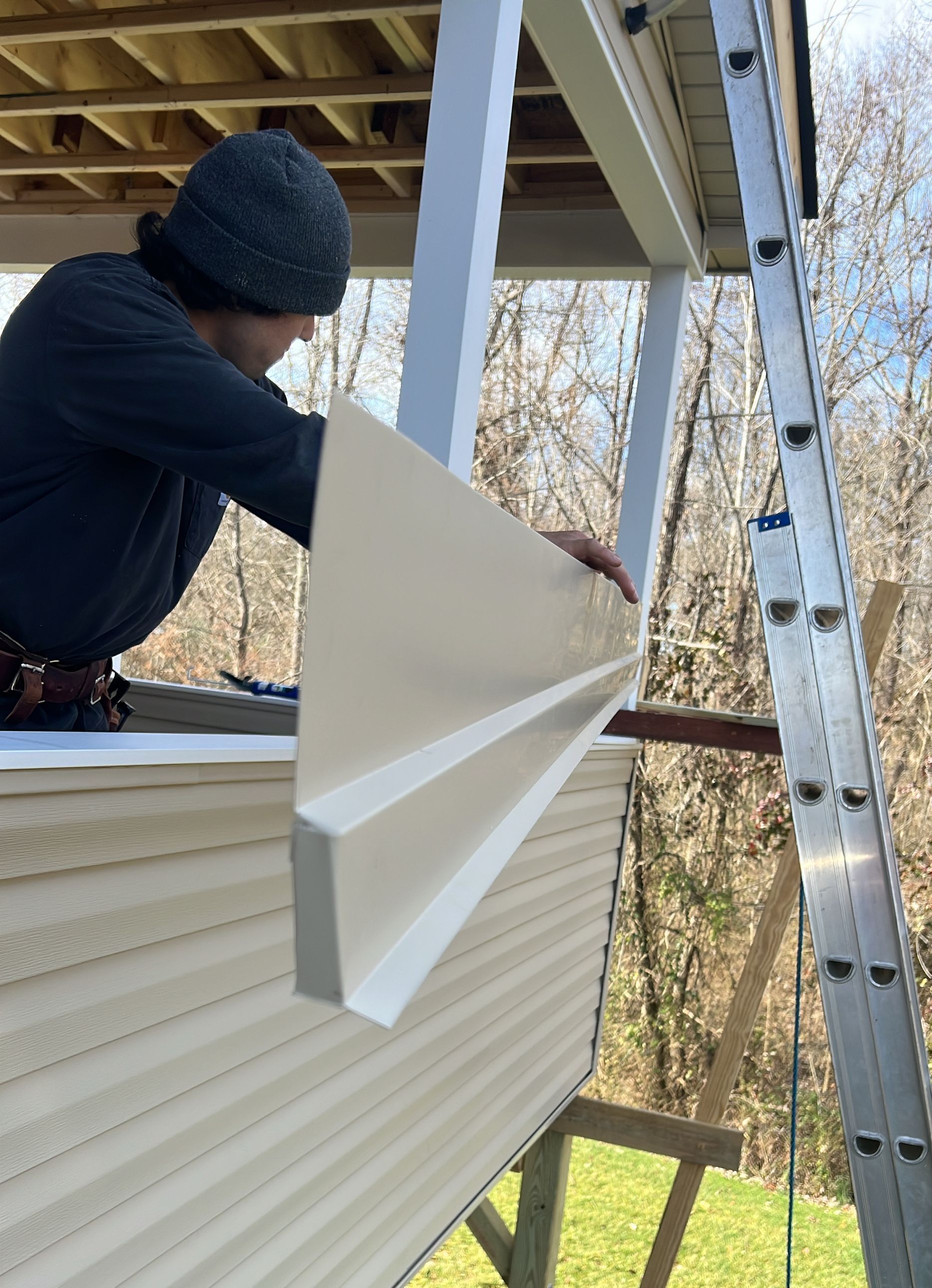 A man is standing on a ladder holding a piece of wood.