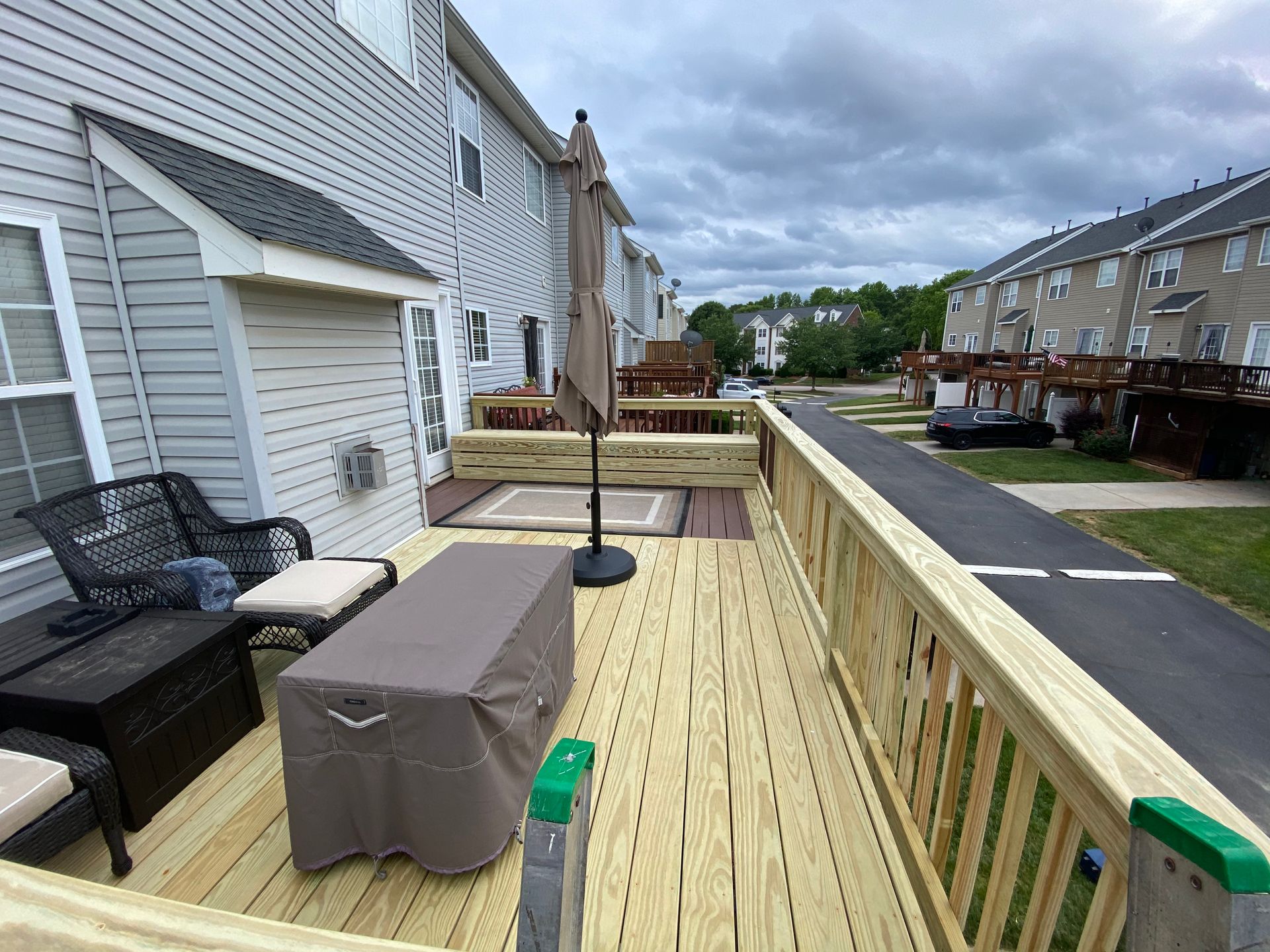 A wooden deck with furniture and an umbrella in front of a house.